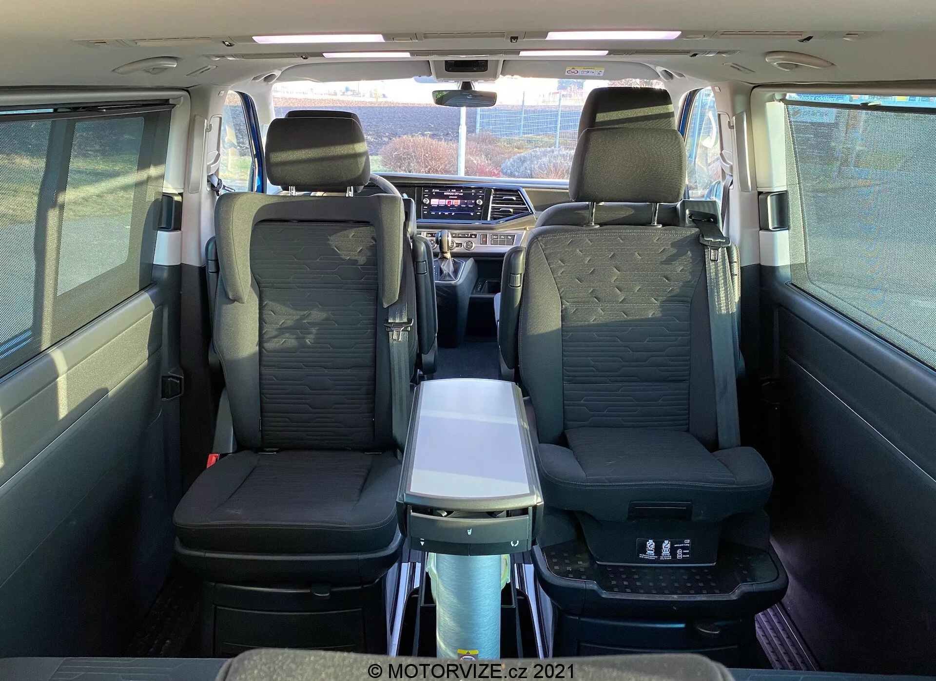 Interior of 2019 VW Nutzfahrzeuge Transporter T6-1 Multivan viewed from the rear, showcasing leather seats, second-row armrests, a folding table, panoramic sunroof, individual air vents, and advanced infotainment system; highlights passenger comfort and spacious cabin.