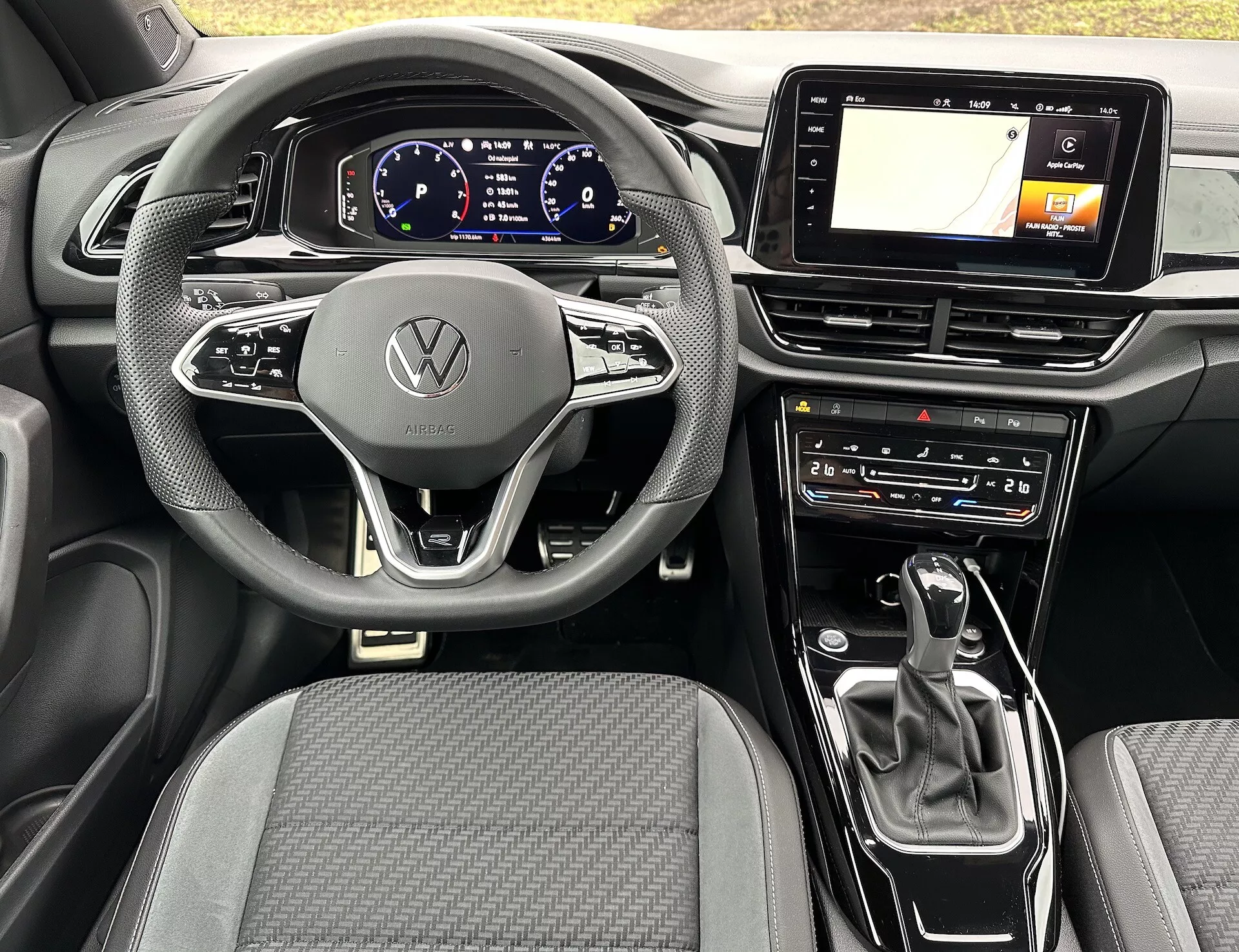 Interior view of the 2022 VW T-Roc Cabriolet featuring a modern three-spoke steering wheel with Volkswagen emblem, digital instrument cluster, GPS-enabled infotainment touchscreen, automatic transmission gear selector, and climate control settings, highlighting the car's advanced technology and sleek design