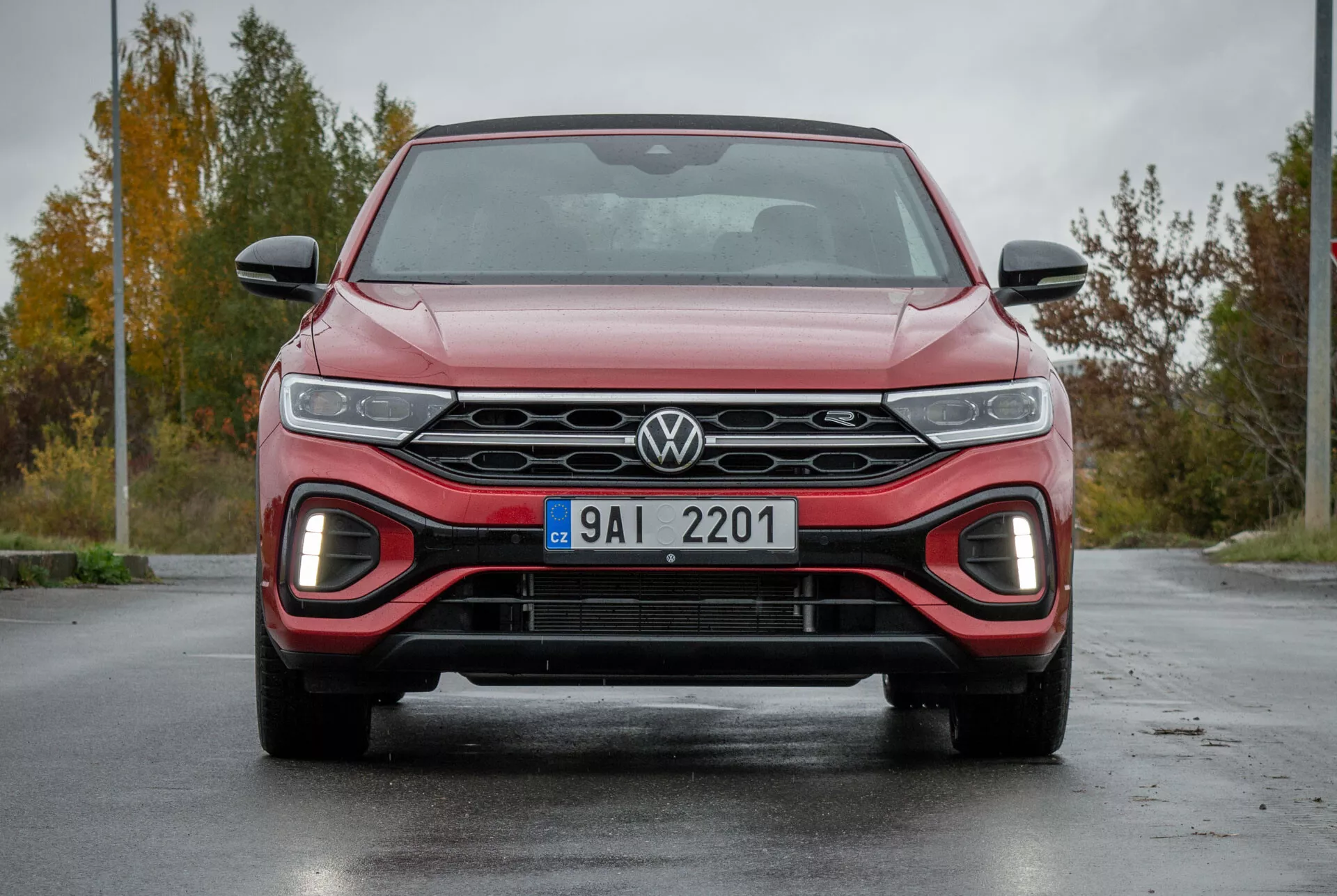 Front view of 2022 VW T-Roc Cabriolet highlighting the sleek grille with Volkswagen logo, LED headlights, red-accented lower air intake for a sporty look, and aerodynamic design on wet pavement
