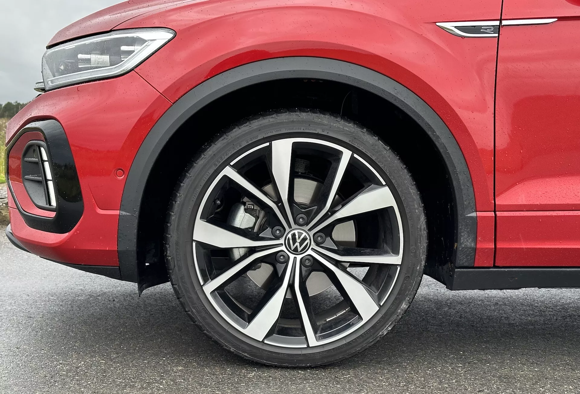 VW T-Roc 2022 close-up focusing on the multi-spoke alloy wheel with two-tone finish, low-profile tire, and partial front quarter panel showcasing sporty red bodywork and LED lighting detail