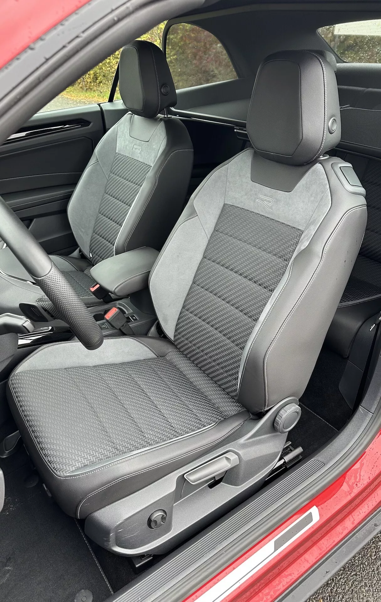 Interior view of a 2022 VW T-Roc Cabriolet focusing on the front driver and passenger seats upholstered with a two-tone fabric, showcasing adjustable headrests, manual seat adjustment controls, and pronounced side bolsters for enhanced support.