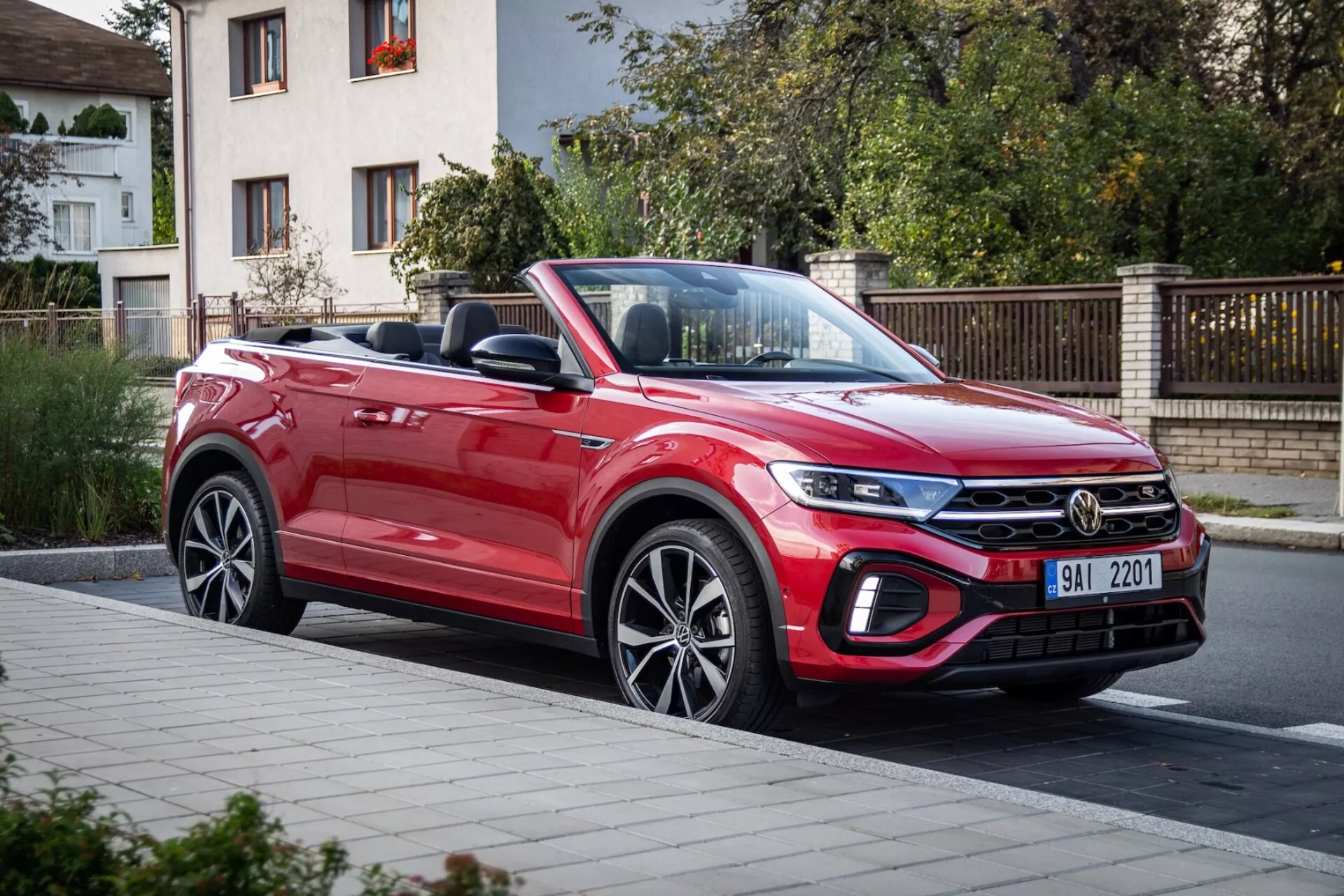 2022 VW T-Roc Cabriolet in red, showcasing its dynamic design with a long sloping hood, modern front grille, sleek headlights, and aerodynamic profile captured in a three-quarter front view on a street