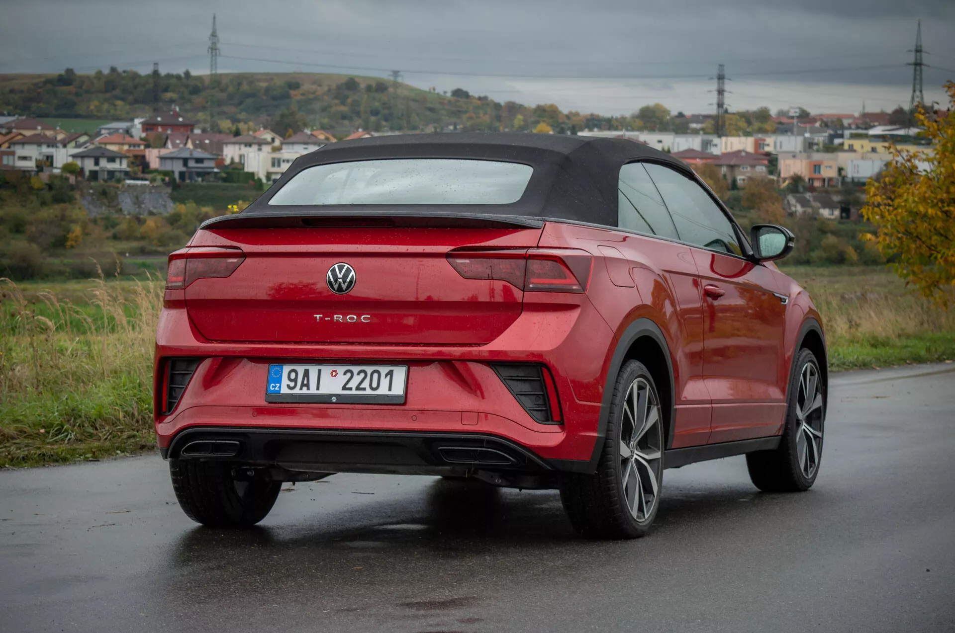 Red Volkswagen T-Roc Cabriolet 2022 in three-quarter rear view on a wet road, showcasing rear design, side profile, wheel design, LED tail lights, rear bumper with integrated sensors, dual exhaust pipes, multi-spoke alloy wheels, and convertible top