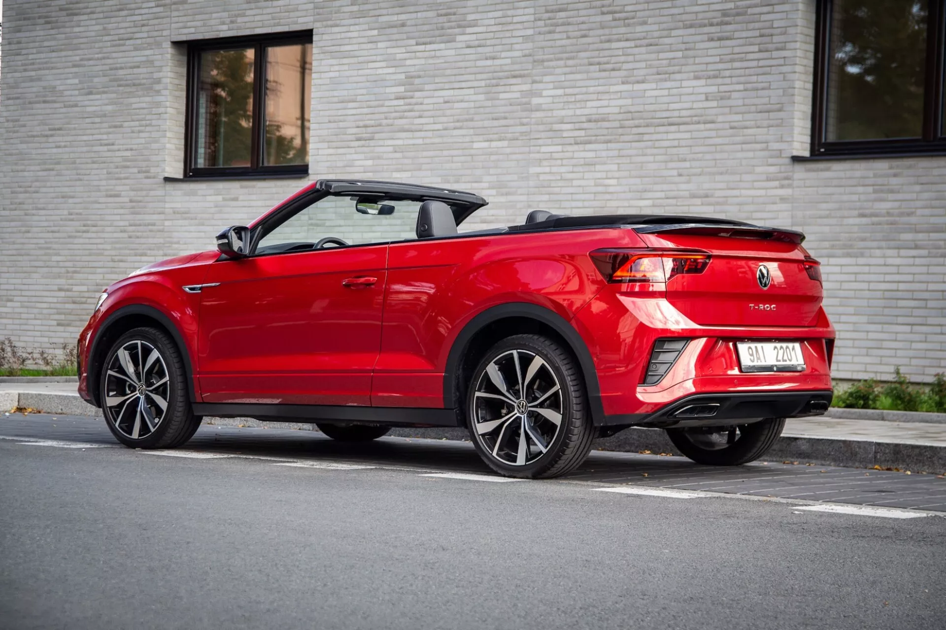 Three-quarter rear view of a red 2022 VW T-Roc Cabriolet with retracted soft-top, showcasing LED taillights, dual exhaust, and multi-spoke alloy wheels, parked on a street under soft daylight