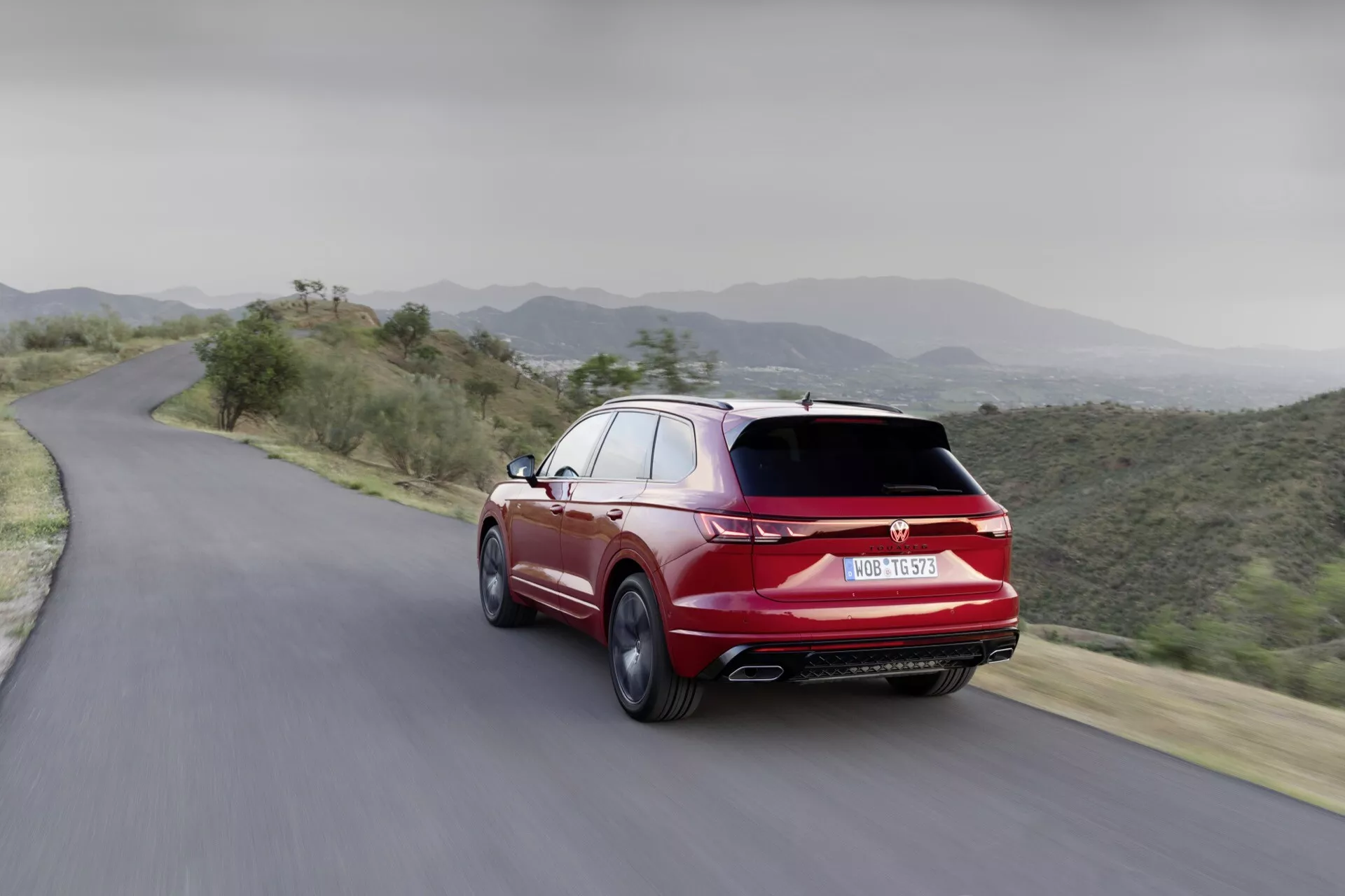 2023 VW Touareg dynamic rear-view on mountain road, showcasing aerodynamic design, dual exhausts, and sporty trim in vibrant red